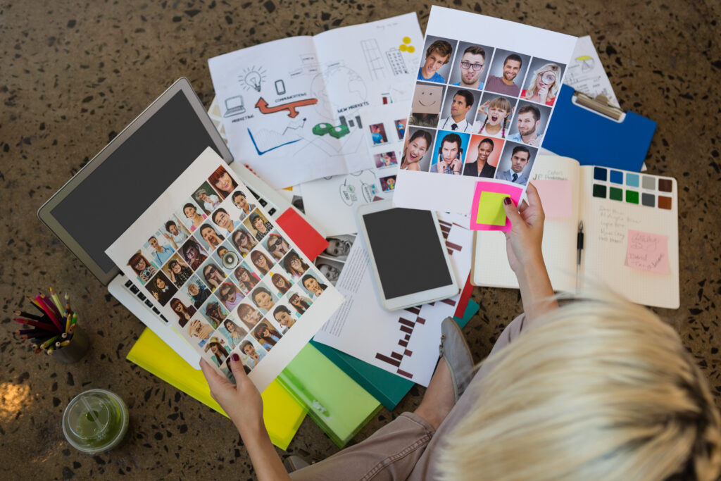 High angle view of young Caucasian businesswoman holding documents sitting on floor at creative office. Documents, laptop, and notebook are displayed on the ground.